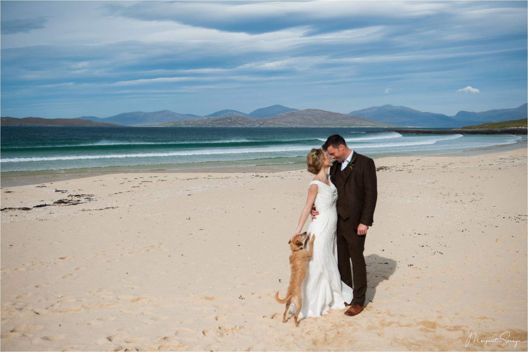 The bride and groom have wedding portraits on Scarista Beach with their dog standing on its hind legs, wanting to be part of the celebrations. 