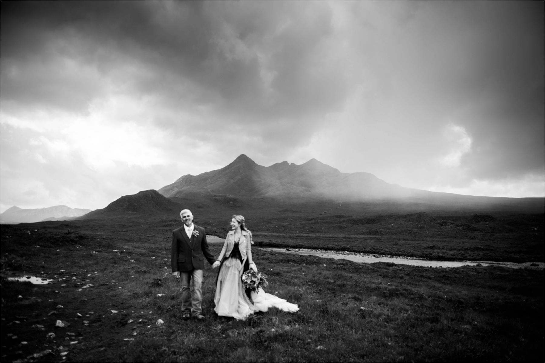 Black and white photo of a bride and groom standing in the Isle of Skye with a storm brewing in the background. 