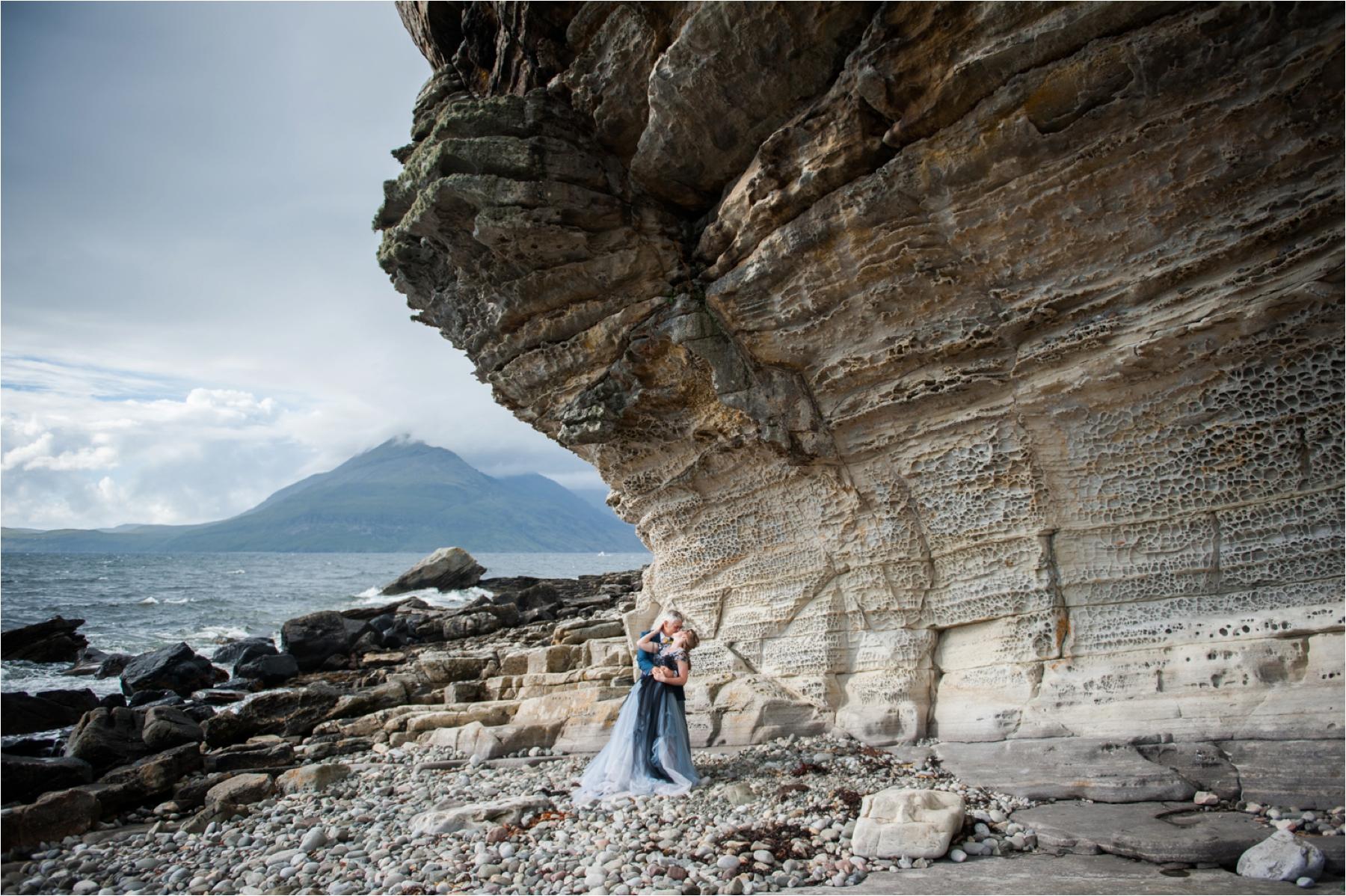 A bride and groom kiss near a dramatic rock formation during their bridal portrait session with photographer Margaret Soraya. 