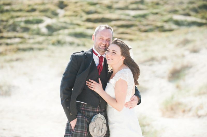 The groom wears a Scottish kilt in tartan and his bride wears cream for their beach wedding in Scotland.