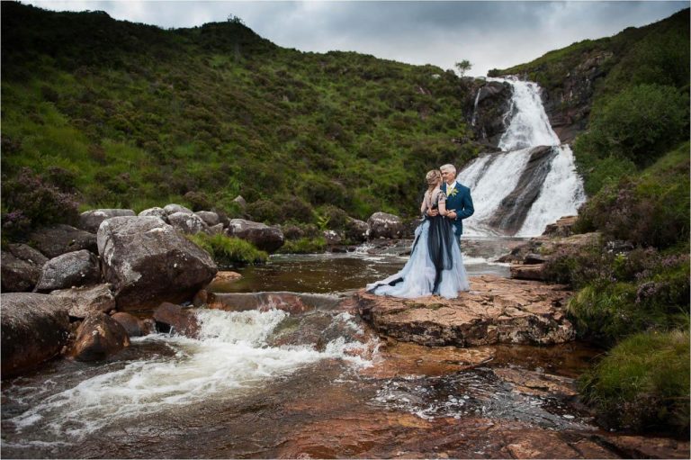 A bride and groom stand near a gushing river for wedding portraits after their Isle of Skye outdoor civil wedding ceremony.