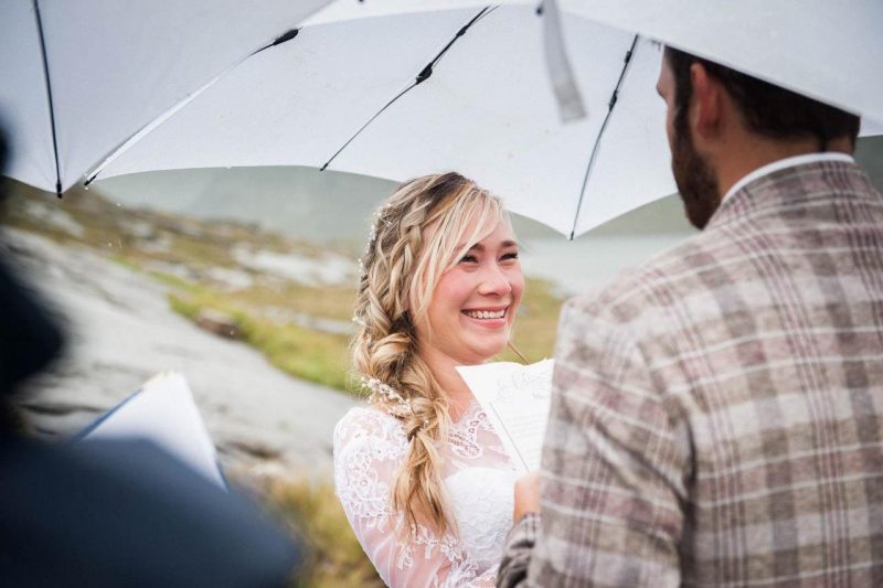 The bride and groom say their vows in an outdoor ceremony on the Isle of Skye in the Scottish Highlands. They're under an umbrella.