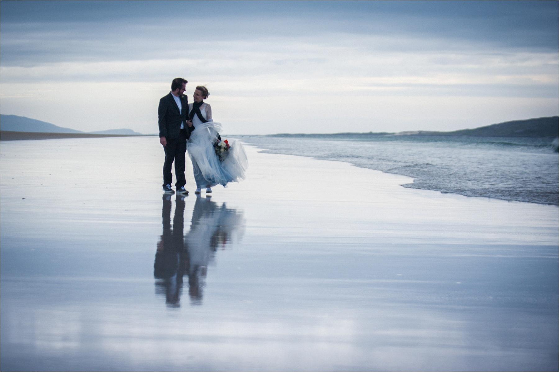 Scarista Beach elopement photo of a bride and groom on a deserted beach, reflected on the wet sand. 