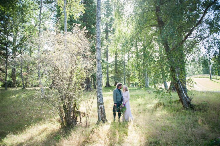 A bride and groom walk through a green field after their Highlands wedding in Scotland.