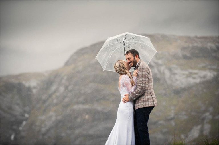 A bride and groom hold each other under a large white umbrella after their Isle of Skye wedding ceremony.