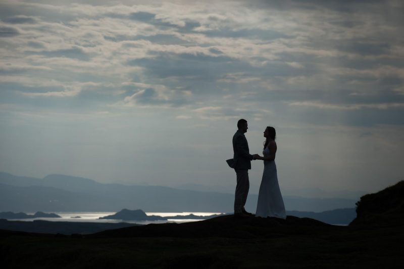 A couple silhouetted against a stormy skyline on the Isle of Skye in Scotland on their wedding day.
