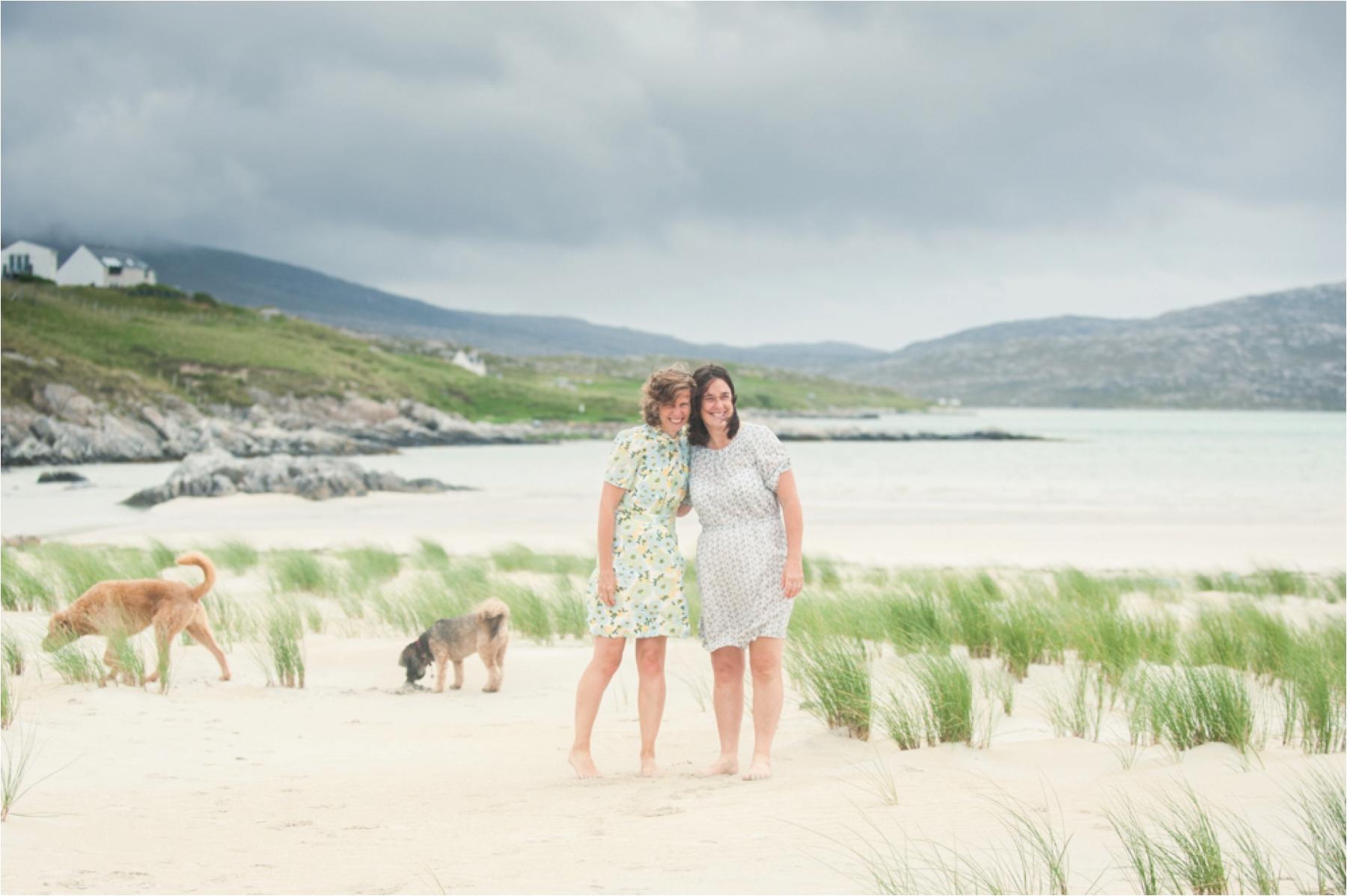 Two brides and their two dogs stand in the sand dunes of Luskentyre Beach on the Isle of Harris for wedding portraits by photographer Margaret Soraya. 