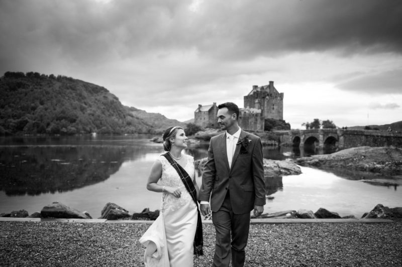 A black and white photo of a bride and groom in front of Eileen Donan Castle on the Isle of Skye.