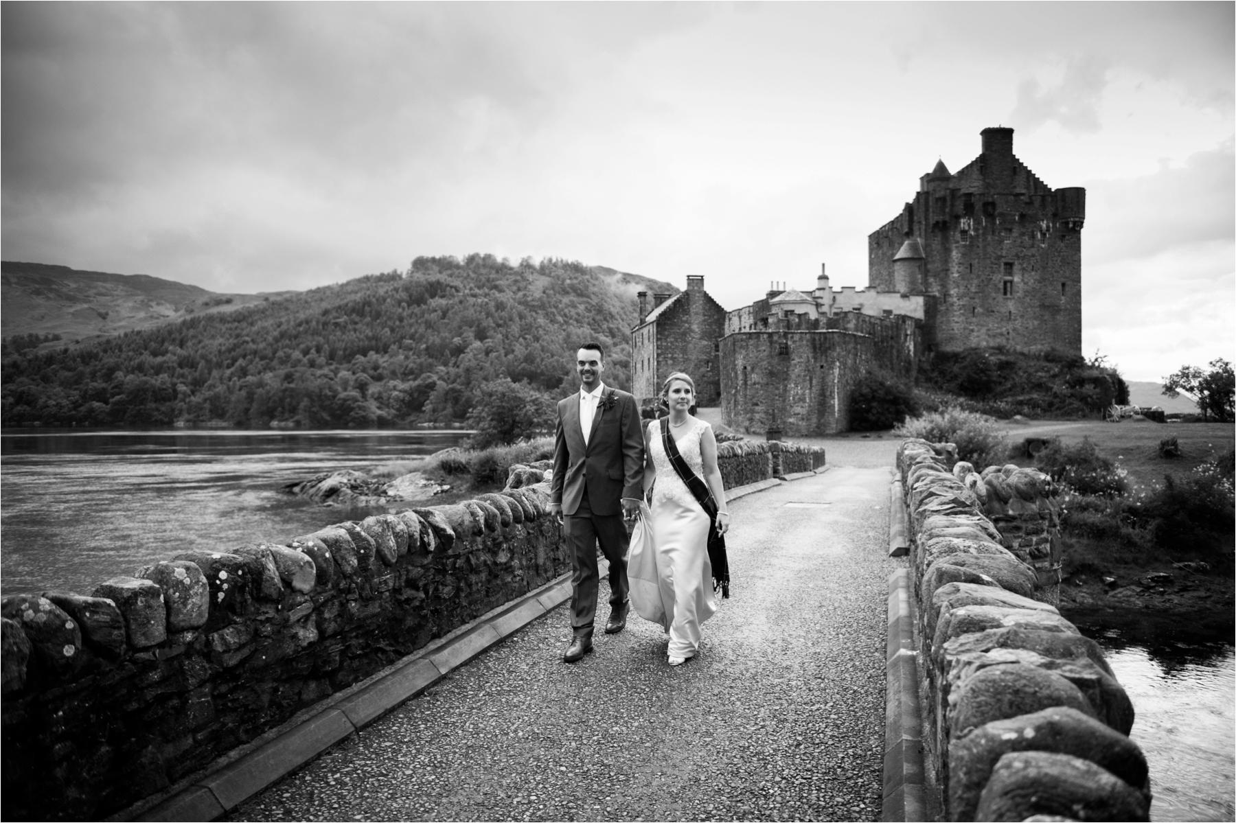 Newlyweds walk over the bridge at Eilean Donan Castle. 